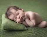 Dolce neonato scatti nel sonno, appoggiato su un cuscino verde. La sua manina è vicino al viso, in un sonno profondo e sereno.