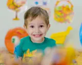 Niño sonriente con camiseta verde, rodeado de materiales educativos. Fomenta la autoestima en niños.