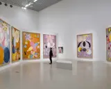 En person betraktar färgglada, abstrakta målningar av Hilma af Klint i ett ljust galleri.
