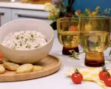 Un bol de rillettes de thon crémeuses, garni de ciboulette, servi avec des crackers, des bâtonnets de carottes et de céleri. Deux verres de vin blanc complètent cette scène gourmande.