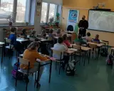 Dzieci słuchają lekcji o bezpieczeństwie w szkole. Nauczycielka i policjant prowadzą zajęcia.