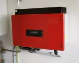 Röd kostal växelriktare monterad på en vit vägg. Enheten har en liten display och indikatorlampor.