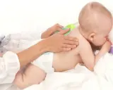 Delikatny masaż pleców niemowlaka, który waży już 9 kg. Ręce opiekuna głaszczą jego plecy.