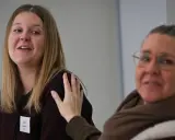 Två kvinnor, en med ett namnskylt där det står "Linda", en annan kvinna lägger en hand på hennes axel. Ingen information om linda hunt sjukdom.