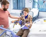 Un homme aide une femme à s'asseoir sur un lève-personne, illustrant l'ergonomie infirmier pour un transfert sécurisé.