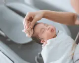 Bain d'un nouveau-né : une main nettoie délicatement la tête du bébé avec une petite serviette. Une scène paisible qui rappelle la liste produits toilette bébé naissance.