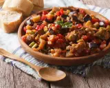 Un plat de caponata, une recette sicilienne savoureuse, garni de basilic frais, servi avec du pain croustillant.