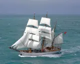 Majestueux voilier 3 mats, ses voiles blanches gonflées par le vent, navigue sur une mer agitée.