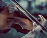 Main d'un musicien jouant du violon, un instrument à cordes, pas à vent. La musique s'élève.