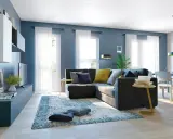 Un soggiorno moderno con divano angolare grigio scuro, cuscini blu e gialli, tappeto blu e bianco. Le pareti blu creano un'atmosfera rilassante, dimostrando che blu e grigio stanno bene insieme.