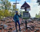 Kobieta na szczycie Łysicy, 614 m n.p.m., z drewnianym krzyżem i drogowskazem szlaku. Jesienne liście i kamienie wokół.