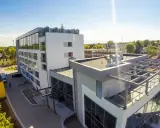 Nowoczesny budynek, gdzie hotel skal właściciel dba o komfort gości. Widać parking, zielone otoczenie i słoneczne niebo.