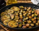 Aubergines sautées dans une poêle, certaines en rondelles, d'autres en dés, parsemées d'herbes fraîches. Un délice à déguster !