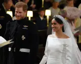Meghan Markle y el Príncipe Harry sonríen en su boda. Ella luce un vestido blanco y él un uniforme militar.