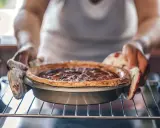 Hände mit Ofenhandschuhen nehmen einen frisch gebackenen Nusskuchen aus dem Ofen. Alles, was man zum Backen braucht: Zutaten, ein Rezept und Geduld.