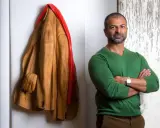 Livio De Marchi, artiste sculpteur, pose à côté de son manteau en bois sculpté, une œuvre saisissante.