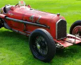 Roter Alfa Romeo P3 Rennwagen mit Nummer 42 fährt auf einer Straße, Fahrer mit Kopftuch.