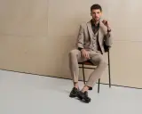 Elegancki mężczyzna w beżowym garniturze, uosabiający włoski styl męski, siedzi na krześle.