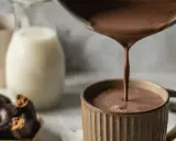Varm choklad hälls upp i en mugg. Bredvid står en skål med chokladkakor och en mjölkflaska.