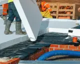 Pracownicy układają płyty styropianowe, wykonując ocieplenie stropu.