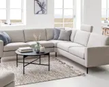 En ljus, modern hörntyp av soffa med kuddar och ett runt soffbord framför.
