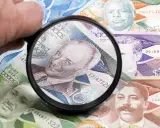 Förstoringsglas granskar sedlar med porträtt, visar Barbados valuta.