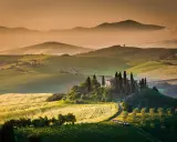Dolci colline verdi e un casale con cipressi nel Val d'Orcia. Ideale da visitare in primavera o autunno per colori e luce perfetti.