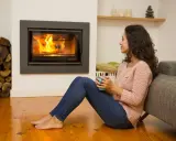 Une femme savoure une boisson chaude près d'une cheminée crépitante, profitant du meilleur chauffage pour une soirée cosy.