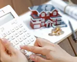 Calculando la casilla 435 renta: una mano usa una calculadora blanca junto a una maqueta de casa, monedas y planos.