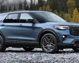 Niebieski Ford Explorer ST zaparkowany na kamienistej plaży, z jesiennym lasem w tle.
