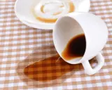 Um Kaffeeflecken aus Tischdecke zu entfernen, braucht es Geduld. Eine umgekippte Tasse hinterließ einen braunen Fleck auf kariertem Stoff.