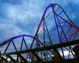 Najwyższy rollercoaster na świecie, oświetlony niebieskim i różowym światłem, wznosi się na tle burzowego nieba.