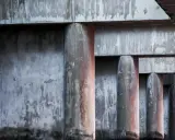 Columnas y vigas de concreto con textura desgastada, creando un patrón rítmico bajo la luz.