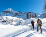 Coppia con ciaspole esplora un sentiero innevato in montagna, un'ottima idea per chi cerca dove ciaspolare in Lombardia.