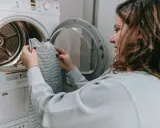 Mujer revisa una prenda antes de meterla a la secadora, pensando en como hacer que encoja la ropa.