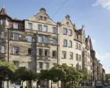 Ein prächtiges Jugendstil Haus mit Erker und Türmchen, umgeben von Bäumen, steht an einer belebten Straße.