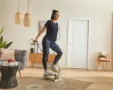 Une femme fait du step à la maison, casque sur les oreilles, pour un entraînement cardio efficace dans son salon.