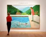 A woman in red observes David Hockney's iconic pool painting at Christie's, a testament to his significant david hockney net worth.