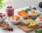 En härlig samling av nyttiga alternativ för ett bra mellanmål: smoothie, kvarg med bär, äggmackor, grönsaksstavar med hummus och nötter.