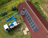Installatörer monterar solpaneler på ett tak med hjälp av en kranbil. Solpaneler omvandlar solljus till likström (DC), som sedan kan omvandlas till växelström (AC) för användning i hemmet.