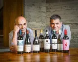 Dos hombres sonríen detrás de una fila de botellas de vino. Uno de ellos es el dueño de Bodegas Olarra.