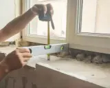 Ręce mierzą taśmą i poziomują, by wiedzieć, jak zmierzyć parapet wewnętrzny.