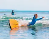 Niño sonriente surfeando en Portugal, una actividad genial que ver en Portugal con niños.