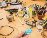 Bastelmaterialien auf Holztisch, darunter Schnur, Federn, Pinsel und eine kleine Flasche uhu super glue.