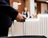 Mężczyzna w garniturze trzyma walizkę, zbliżając się do recepcji hotelowej. Czas na depozyt w hotelu i nowy początek podróży.