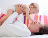 Mama podnosi dziecko, które wyciąga rączkę do jej nosa. Zdjęcie symbolizuje troskę o rozwój malucha, jak omega 3 dla niemowląt.