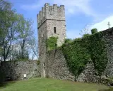 Antica torre del forte di Orino, circondata da mura in pietra e vegetazione rigogliosa, sotto un cielo azzurro.