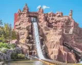 Aventura acuática en uno de los parques de atracciones en España. Un tronco desciende por una cascada artificial en un paisaje rocoso.