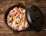 Dutch oven mit Fleisch, Kartoffeln und Zwiebeln, bereit für köstliche Dutch Oven Rezepte auf dem Gasgrill.