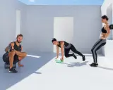 Drei Sportler nutzen eine **blackroll vor oder nach dem Training**. Ein Mann dehnt sich, eine Frau macht Mountain Climbers, die andere lehnt sich an die Wand.